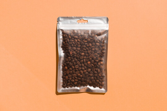 Blank craft plastic pouch mock up with coffee beans inside, transparent pack on studio background with shadow, mylar bag isolated for coffee product