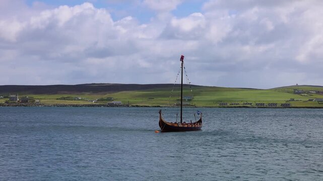 Traditional wooden Viking ship floating in clear bay waters near Lerwick Shetland Islands with green rolling hills behind