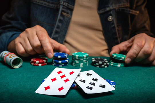 A gamester sits at a poker table, focusing on his hand of cards. Several stacks of poker chips are arranged in front of him, creating a competitive atmosphere in the room