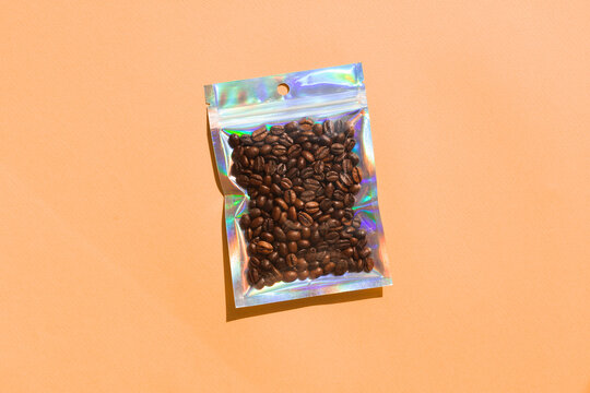 Blank craft plastic pouch mock up with coffee beans inside, transparent pack on studio background with shadow, mylar bag isolated for coffee product