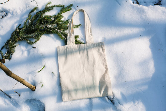 White cotton mesh bag on winter snow with fir tree branches background. Zero waste, no plastic, eco friendly shopping, recycling, christmas concept. Blank mockup, place for text. copy space flat lay