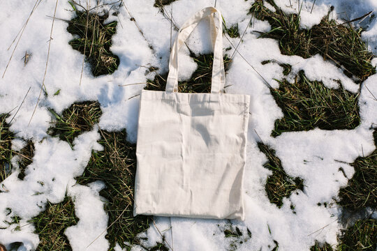 White cotton mesh bag on spring snow, green grass thawed patches background. Zero waste, no plastic, eco friendly shopping, recycling concept. Blank mockup shopper, place for text. copy space flat lay