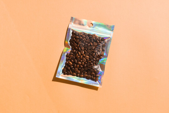 Blank craft plastic pouch mock up with coffee beans inside, transparent pack on studio background with shadow, mylar bag isolated for coffee product