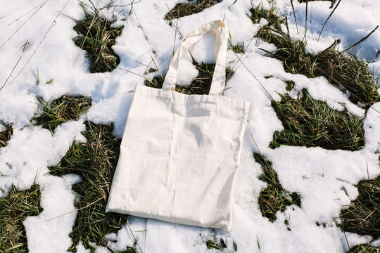White cotton mesh bag on spring snow, green grass thawed patches background. Zero waste, no plastic, eco friendly shopping, recycling concept. Blank mockup shopper, place for text. copy space flat lay