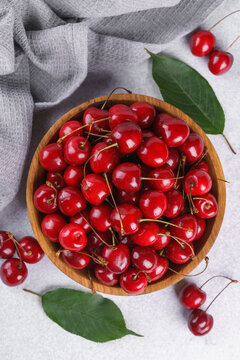 Fresh ripe red sweet cherries in wooden bowl with green leaves on light textured background. Healthy organic summer fruit, juicy red berries, natural freshness, healthy eating, seasonal food