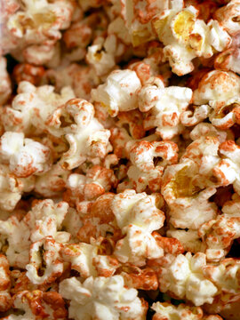 A close-up shot of popcorn coated in spices. The popcorn is a mix of white and red, with some kernels visible.