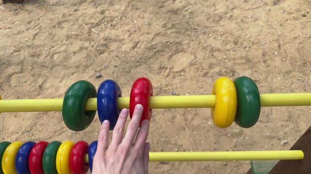Child hand moving colorful beads on yellow abacus at sandy playground outdoors. Learning to count, early education, kids development, outdoor play
