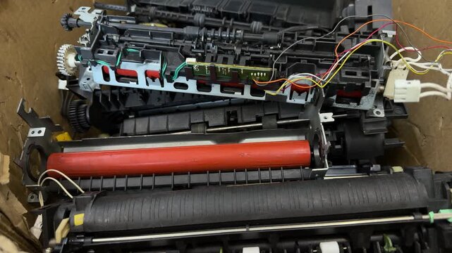 Disassembled printer parts with rollers, gears and wires in cardboard box. Repair workshop, spare parts, office equipment maintenance, recycling