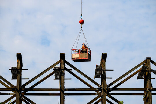 Construction workers in arial work basket over old tall wooden railroad trestle, train tracks removed, structural framework update, sunny summer day, America
