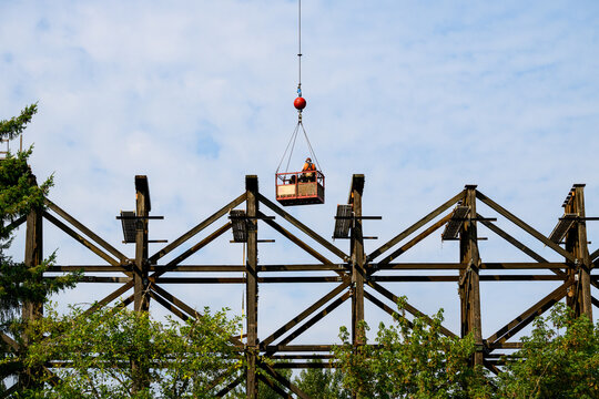 Construction workers in arial work basket over old tall wooden railroad trestle, train tracks removed, structural framework update, sunny summer day, America
