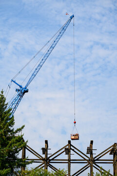 Workman in work basket help aloft by blue crane, old wood railway train trestle construction project to update structural framework, sunny summer transportation project, United States

