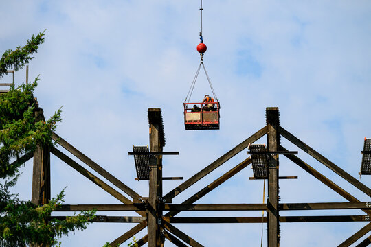 Construction workers in arial work basket over old tall wooden railroad trestle, train tracks removed, structural framework update, sunny summer day, America
