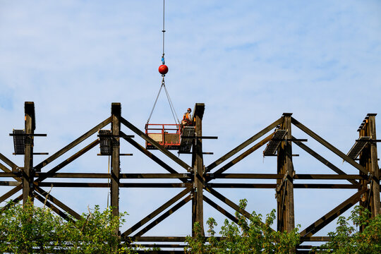 Worker in safety equipment in work on scaffolding overhead, old wood railway train trestle construction project to update structural framework, sunny summer transportation project, United States
