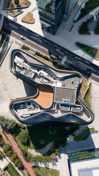 Aerial view of the futuristic U15 office building in Milanofiori Nord with its unique curved architecture, rooftop HVAC systems, and surrounding paved paths in Assago, Lombardy, Italy.