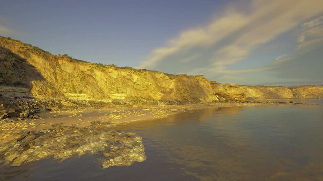 dramatic cliffs at sunset with waves creating motion against rugged shoreline, chalk face glowing in low light, brooding clouds adding contrast, distant horizon
