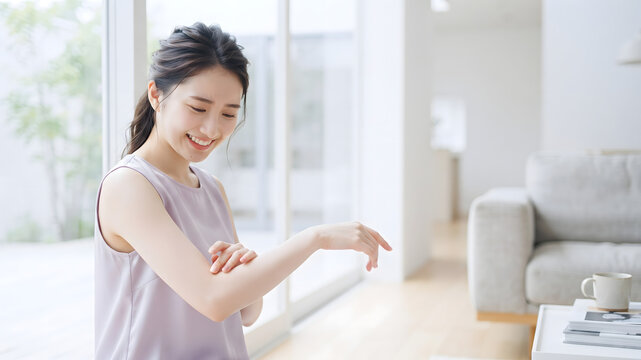 明るい窓際で笑顔で腕の肌を優しくケアする女性のスキンケアイメージ