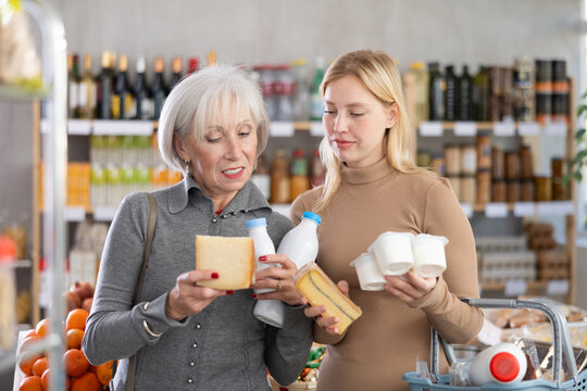 Girl and grandma with dairy products chooses something else, examines labels of cheese yogurt, interested in composition and expiration date. Client examines packaging, looking for something for snack