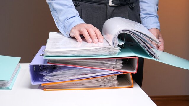 Person arranging paperwork in file folders and ring binders, demonstrating a concept of administrative work, organization, and efficient archival management in an office environment