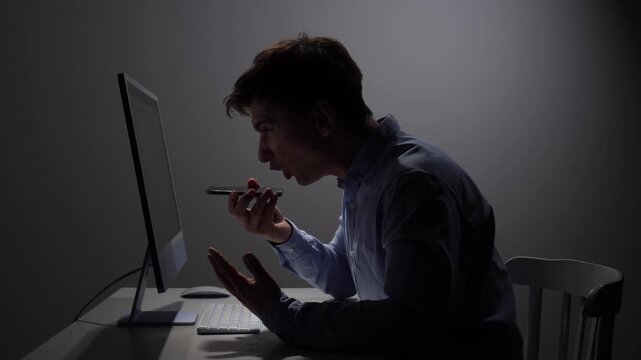 Angry man sitting in dark office yelling into a mobile phone, experiencing intense frustration, rage, and stress from a challenging situation or conversation
