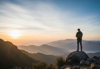 Fototapeta premium Man Standing Alone on Mountain Peak Overlooking Valley at Sunrise