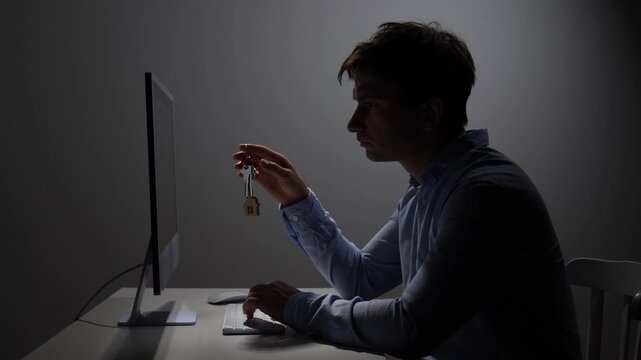 Man holding a small house keychain in front of a computer screen, symbolizing the digital search for a new home, property investment, and online real estate market opportunities