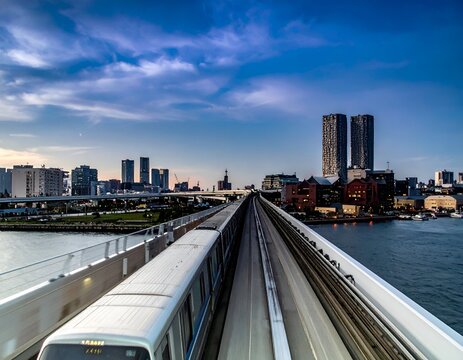 Elevated train track leading towards distant city skyline with twin towers under a twilight sky