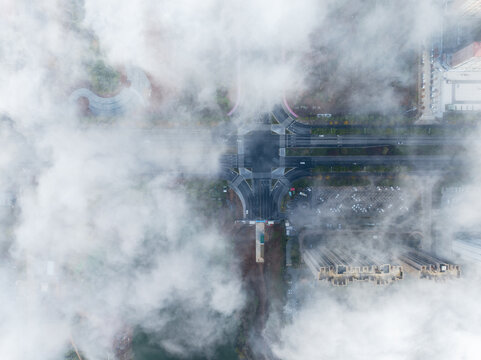 A top-down aerial shot of a city road intersection partially covered by dense mist, showing urban infrastructure.