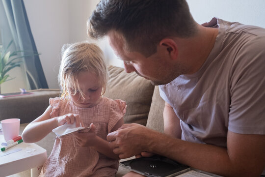 Father and his curious little daughter sitting on a couch while the man cleans a compact disc 