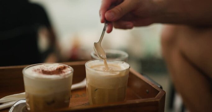 Savoring the unique taste of Vietnam's salted coffee, a beloved traditional beverage, as a hand gently stirs its creamy, rich layers in a cozy cafe setting.