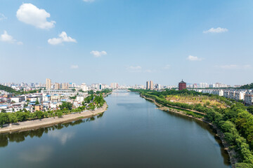 Obraz premium A panoramic view of a riverside city with buildings, green trees, and a pagoda under a clear blue sky.