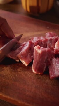 Close-up of a hand holding a pork rib cleaver on a wooden cutting board.
