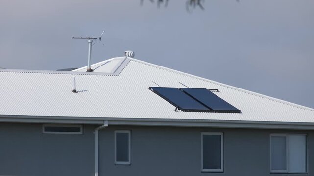Solar hot water collector panels mounted on the pitched corrugated metal roof of a modern residential home, accompanied by a television antenna and roof whirlybird ventilator in Melbourne Australia.