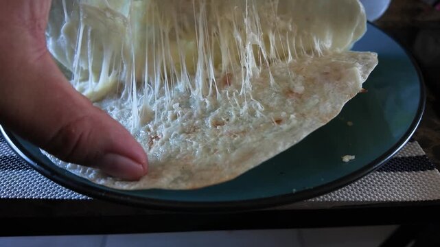 Hand stretching delicious quesadilla with melted stringy cheese in slow motion