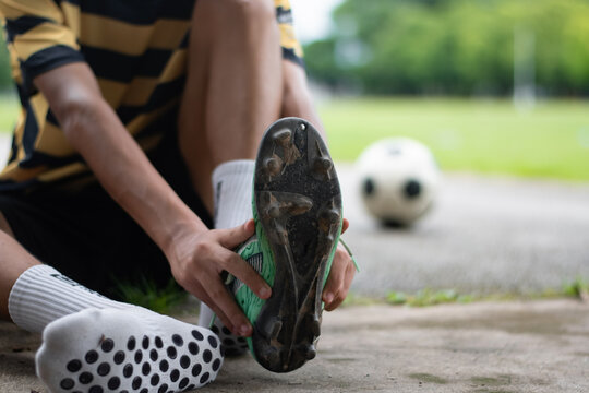 Close-up of a soccer player holding a football boot showing cleats sole and anti-slip grip socks on the ground.