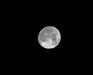 A close-up of a nearly full moon with clear surface details, including craters and dark plains against a dark night sky. © Riza faryunanda