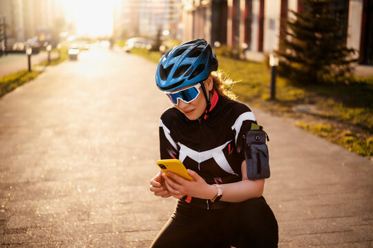 Tired cyclist resting and using smartphone application on urban street