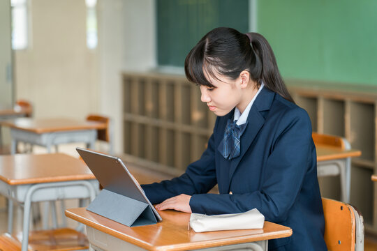 Female middle and high school students in uniform studying using computers and tablets.