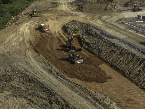 Aerial view of a dump truck, crawler bulldozer, and hydraulic excavator moving and dumping dirt on a construction site in Mt. Juliet, Tennessee, United States.