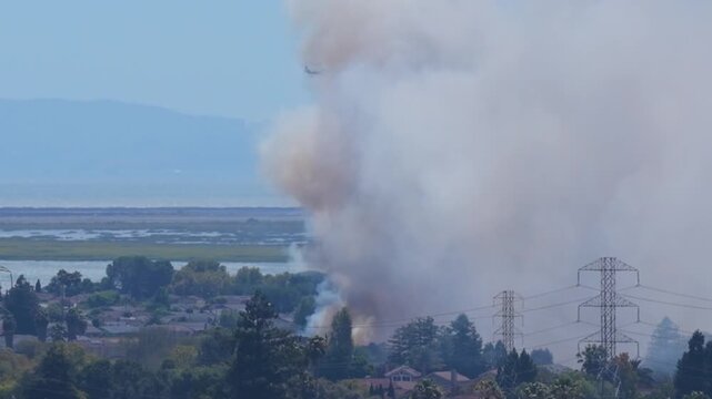 AMERICAN CANYON, CA - JULY 25, 2026: A wildfire smoke column rises between high voltage transmission towers above tidal wetlands and San Pablo Bay during the Dutch Flat Fire, California.