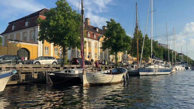 Gliding past traditional yellow heritage buildings and moored wooden sailboats during golden hour in Christianshavn Copenhagen.