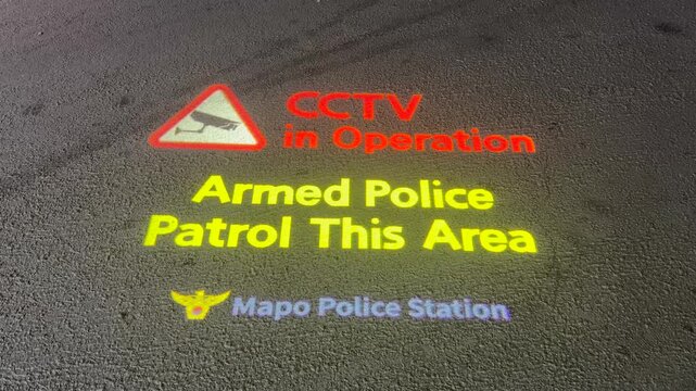 Projected Light Warning Sign On A Sidewalk For CCTV In Operation And Armed Police Patrol In Seoul South Korea