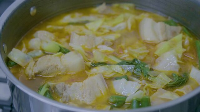 Cooking Filipino Pochero with pork, vegetables, and broth in a pot on a stove