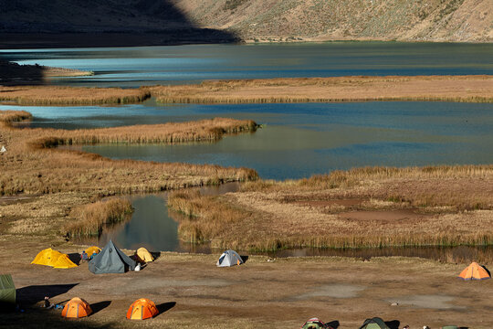 colorful tents rests peacefully on golden grassland at Jahuacocha campsite, dwarfed by the towering, glaciated face of Jirishanca deep in Peru's Cordillera Huayhuash