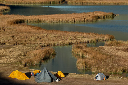 colorful tents rests peacefully on golden grassland at Jahuacocha campsite, dwarfed by the towering, glaciated face of Jirishanca deep in Peru's Cordillera Huayhuash