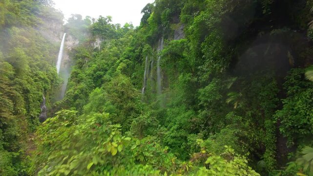 FPV drone flight through a lush rainforest canyon in Costa Rica passing tall waterfalls cascading down mossy cliffs surrounded by dense green tropical foliage and drifting mist.