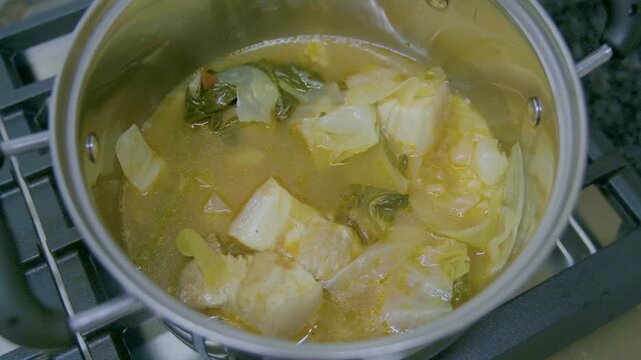 Cooking Filipino Pochero with pork, vegetables, and broth in a pot on a stove