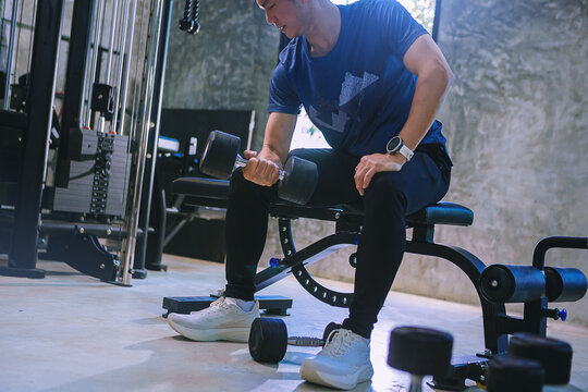 Young man with sweat doing exercises, working out with dumbbell in fitness gym. Strong and healthy concept. Selected focus
