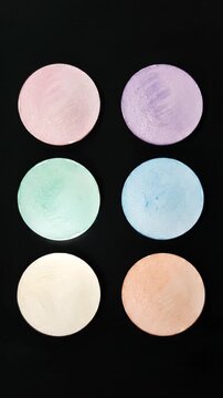 Colorful oval makeup powder samples arranged in two columns on black background