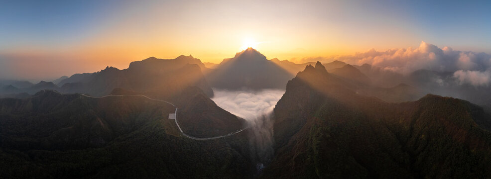 Aerial view of Gunung Kelud at sunrise, with golden light rays illuminating the mountain peaks and a sea of clouds filling the valley below in Kecamatan Ngancar, Jawa Timur, Indonesia.
