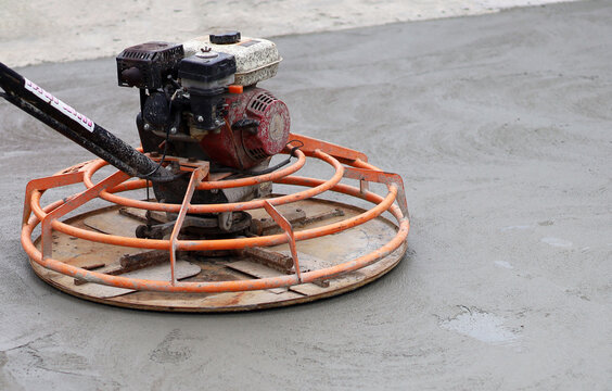 An orange power trowel machine finishing a fresh wet concrete surface on a road construction site.